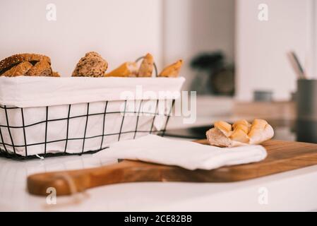Side view of fresh assorted cut bread and buns served in tray and on wooden cutting board on white table during breakfast Stock Photo