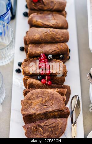 From above of delicious homemade chocolate pancakes garnishes with black and red currants and served on plate Stock Photo