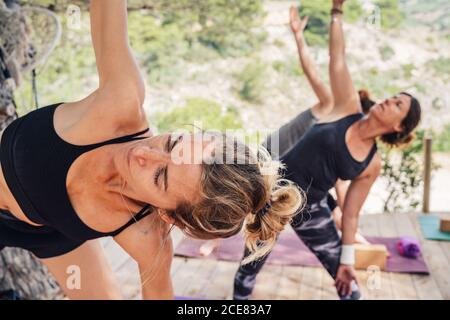 Active women in sportswear attending yoga class in park and performing Parsvakonasana position on sunny day Stock Photo