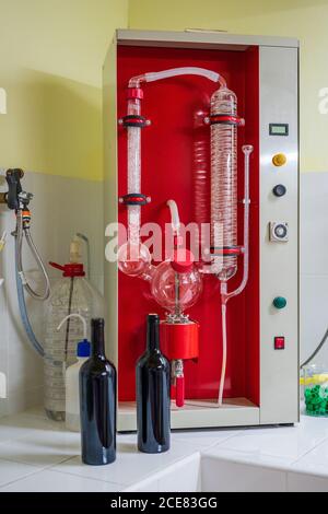 Big rectangular wine analysis equipment with transparent tubes on ceramic surface near similar bottles of red wine in laboratory Stock Photo