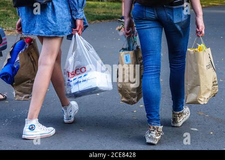 Two young women carrying shopping bags from the supermarket One plastic bag paper bags for recycling. Together walking away shopping bags supermarket Stock Photo