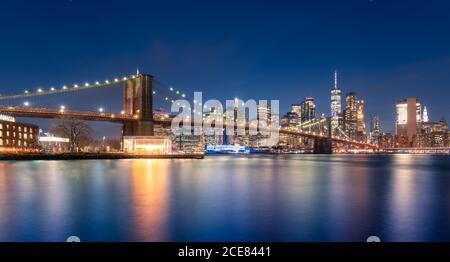 Amazing view of illuminated Brooklyn bridge and glowing skyscrapers with lights reflected in water in night New York City Stock Photo