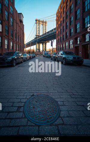 Manhattan bridge seen from narrow paved street of Brooklyn district with old buildings in New York City Stock Photo