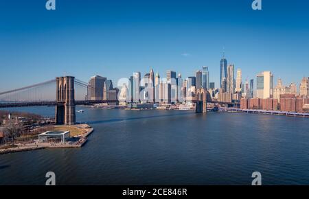 Amazing New York city skyline with famous Brooklyn bridge over river against cloudless blue sky in sunny day Stock Photo