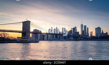 Amazing New York city skyline with famous Brooklyn bridge over river against cloudless blue sky in sunny day Stock Photo