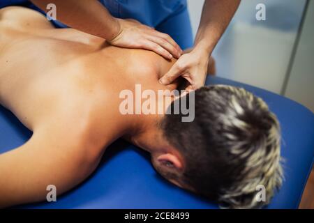 Osteopath in blue uniform examining back of unrecognizable slim male patient with dyed hair lying on examination table in clinic Stock Photo