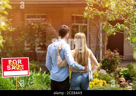 Back view of young couple standing in front yard of their new house, outside Stock Photo