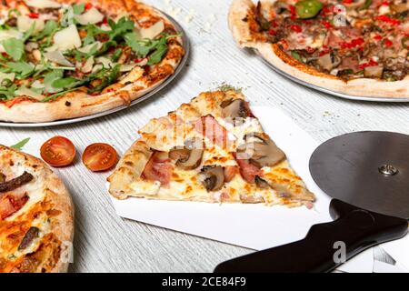 Top view of delicious pizzas with various meat and vegetables placed on white wooden table in cafe Stock Photo