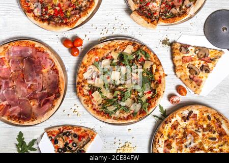 Top view of delicious pizzas with various meat and vegetables placed on white wooden table in cafe Stock Photo