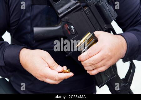 Crop chubby anonymous police officer in dark uniform showing golden bullet made of lead and brass materials while holding firearm in daylight Stock Photo