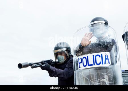 Low angle of swat soldiers in protective uniforms and medical masks armed with assault rifle and riot shield and ready for fight Stock Photo