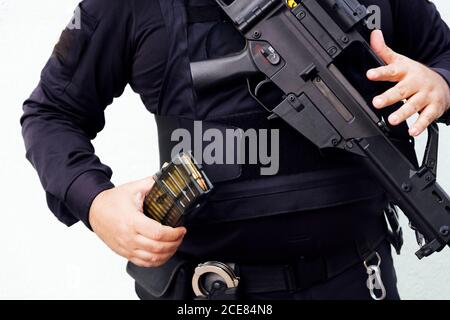 Crop chubby anonymous police officer in dark uniform showing golden bullet made of lead and brass materials while holding firearm in daylight Stock Photo