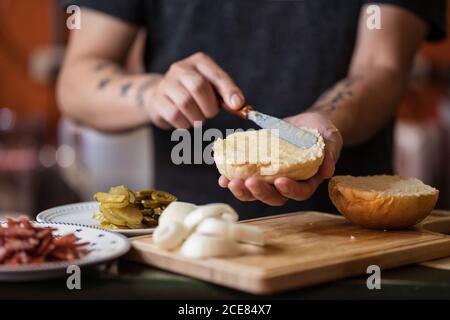unrecognizable male chef standing at table and preparing delicious burgers while spreading butter on bread Stock Photo