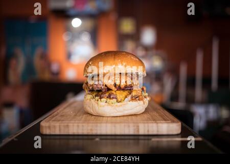 Delicious burger with cutlet and vegetables served on wooden cutting board in cafe Stock Photo