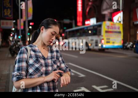 Side view of crop anonymous female in casual checkered shirt checking time on smart bracelet Stock Photo