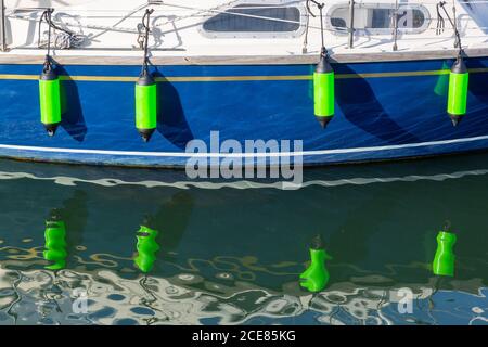 yachts rubber fenders hanging over the side reflecting on the water in a marina Stock Photo