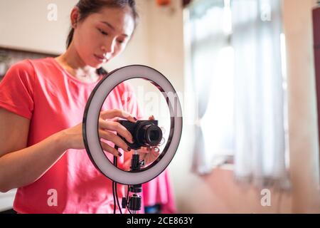Focused young Asian Woman stetting camera on tripod with ring light while preparing for creating new beauty blog at home Stock Photo
