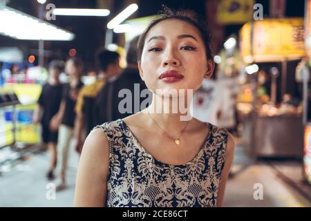 Confident ethnic female standing on crowded street in Night Market in Taiwan and looking at camera Stock Photo