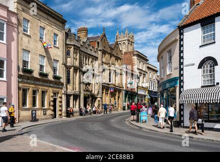 Pedestrians walk past shops, pubs and cafes in the old buildings of High Street and Market Place in the centre of the English town of Glastonbury. Stock Photo
