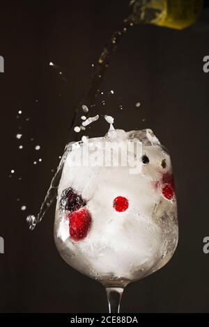 Refreshing transparent cocktail with sparkling water in glass of ice and berries on dark background Stock Photo