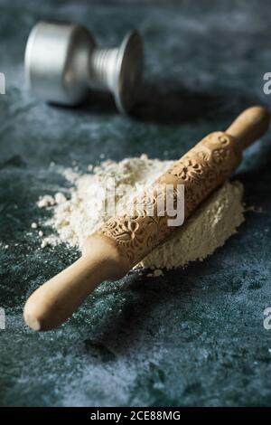 From above of composition of white flower with wooden rolling pin with floral decoration on surface near fallen bowl on dark stone table Stock Photo