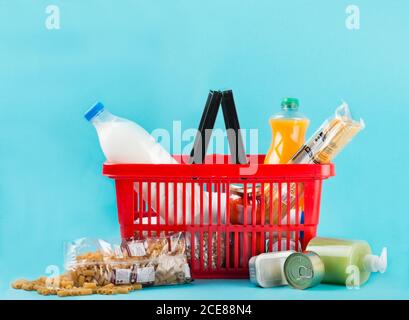 Red plastic shopping basket with fresh groceries in packages placed on light blue background in studio Stock Photo