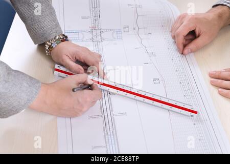 High angle side view of anonymous professional architects making marks on blueprint while working in modern office Stock Photo