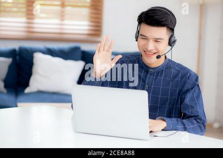 Young asian businessman working on laptop computer wearing headphone at home, business man wearing headset for video conference, communication and edu Stock Photo