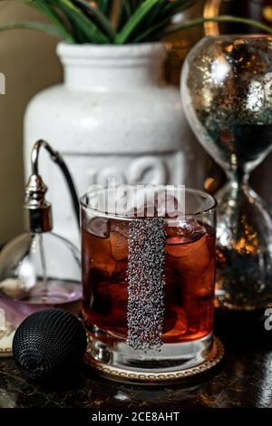 Glass cup of cold alcohol beverage decorated with poppy seeds and placed on table near vintage accessories Stock Photo
