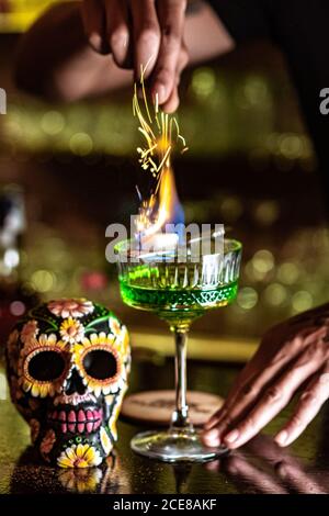 unrecognizable crop barman standing at counter in bar and burning green alcohol drink Stock Photo