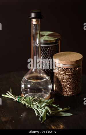 Bunch of fresh herbs placed on table near bottle of vinegar and jars with spices on black background Stock Photo