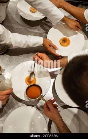 From above unrecognizable male chefs putting sauce on top of exquisite dish while working in luxury restaurant Stock Photo