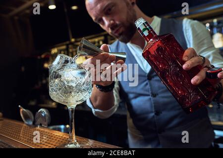 Professional young barman pouring alcohol cocktail from jigger into a glass on counter making beverage working in bar Stock Photo