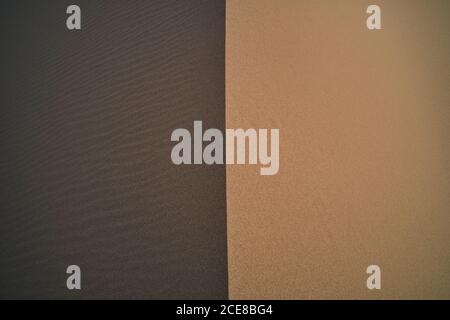 From above of abstract background of light brown sand with smooth dry surface near dark brown rippled terrain with loose texture in desert Stock Photo
