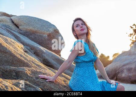 Low angle of Woman traveler in summer dress posing on rough rock near sea during summer holidays Stock Photo