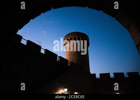 From below of historic brick tower seen from arched passage against blue sky at evening time in Tossa de Mar in Catalonia Stock Photo