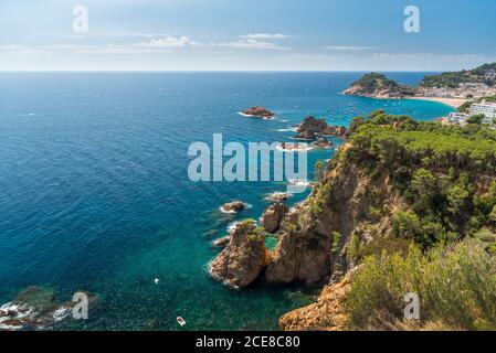 Magnificent drone view of coastline with rocky cliffs covered with green plants and calm sea with turquoise water in sunny summer day in Tossa de Mar in Spain Stock Photo