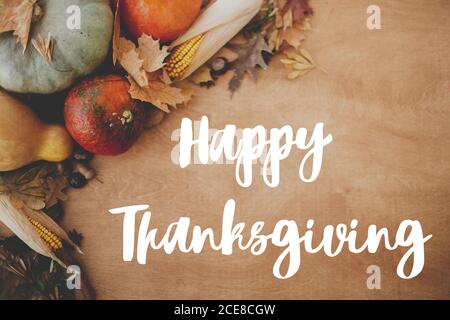 Hand written Happy Thanksgiving text on background of pumpkins, autumn leaves, nuts, harvest vegetables on rustic wood, flat lay. Happy Thanksgiving g Stock Photo