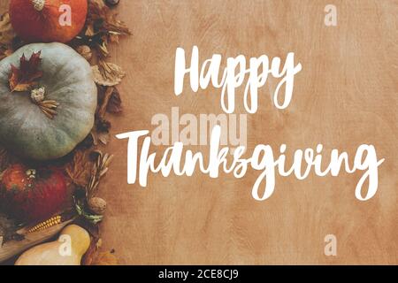 Hand written Happy Thanksgiving text on background of pumpkins, autumn leaves, nuts, harvest vegetables on rustic wood, flat lay. Happy Thanksgiving g Stock Photo