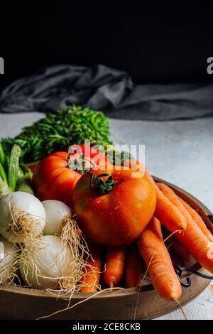 Various fresh vegetables and greens composed on shabby wooden tray on concrete gray table during healthy food preparation Stock Photo