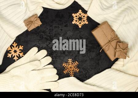 Christmas composition. White scarf, gloves, gift boxes wrapped with kraft paper, wooden snowflakes on black background. Christmas, New Year concept Stock Photo