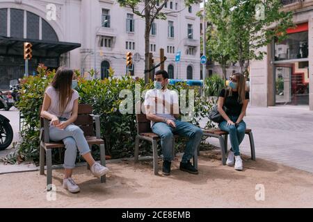 Three friends talking and having fun at the park outdoors wearing face masks and respecting social distancing during a pandemic Stock Photo