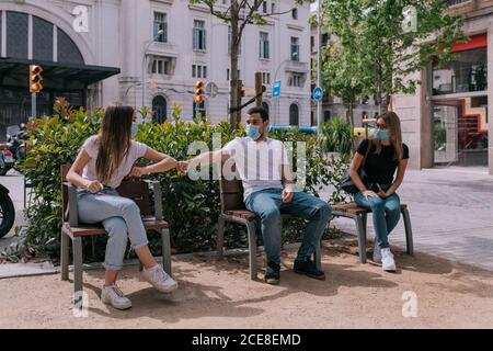 Three friends talking and having fun at the park outdoors wearing face masks and respecting social distancing during a pandemic Stock Photo