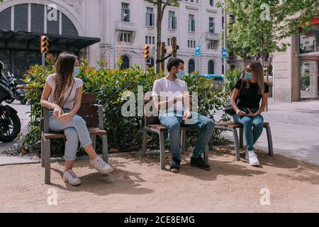 Three friends talking and having fun at the park outdoors wearing face masks and respecting social distancing during a pandemic Stock Photo