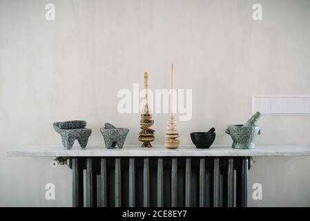 Various kitchen utensils including mortars with pestles arranged in row on marble counter near wall Stock Photo