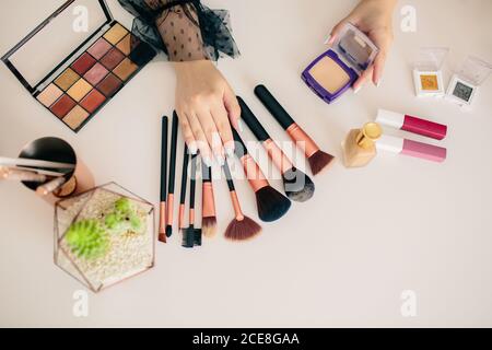 Crop makeup artist demonstrating various beauty products and accessories placed on table in beauty salon Stock Photo
