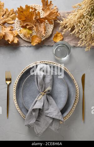 Autumn table setting with dry yellow oak leaves, fall decoration and golden cutlery on grey. Thankisgiving day Stock Photo