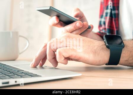 Freelancer using smartphone and laptop computer in home office while telecommuting, selective focus Stock Photo
