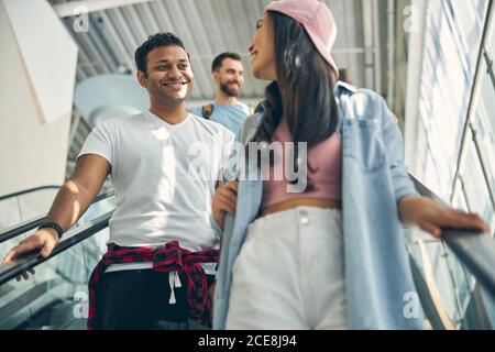 Handsome Indian male listening stylish woman while standing on moving staircase Stock Photo