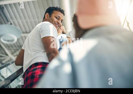 Handsome Indian man in white shirt standing on the moving staircase and looking to her friends Stock Photo